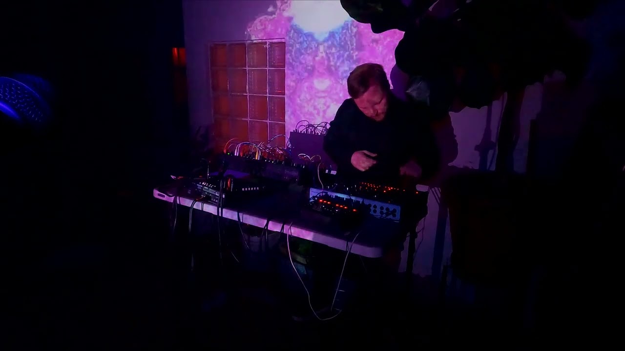Performer at keyboards on a dark stage with purple light